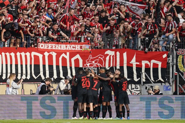 Leverkusen's players celebrate beneath supporters after their teammate Alejandro Grimaldo scored their side's second goal during a German Bundesliga soccer match between FSV Mainz 05 and Bayer Leverkusen, at the Mewa Arena in Mainz, Germany, Saturday Sept. 30, 2023. (Uwe Anspach/dpa via AP)