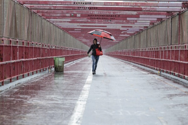 A person walks over the Williamsburg Bridge with an umbrella on Friday, Sept. 29, 2023 in New York. A potent rush-hour rainstorm swamped the New York metropolitan area on Friday, shutting down some subways and commuter railroads, flooding streets and highways, and delaying flights into LaGuardia Airport. (AP Photo/Stefan Jeremiah)