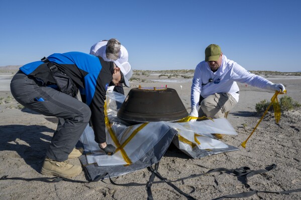 In this photo provided by NASA, from left, Lockheed Martin Mission Operations Assurance Lead Graham Miller, Lockheed Martin Recovery Specialist Michael Kaye, and Lockheed Martin Recovery Specialist Levi Hanish, prepare the sample return capsule from NASA's Osiris-Rex mission for transport after it landed at the Department of Defense's Utah Test and Training Range on Sunday, Sept. 24, 2023. The sample was collected from the asteroid Bennu in October 2020. (Keegan Barber/NASA via AP)