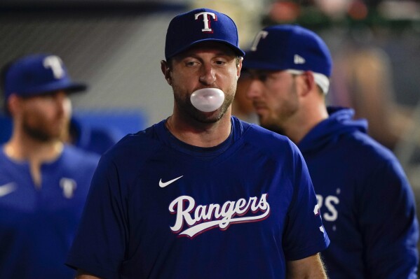 Texas Rangers pitcher Max Scherzer blows a gum bubble in the dugout during the second inning of a baseball game against the Los Angeles Angels, Monday, Sept. 25, 2023, in Anaheim, Calif. (AP Photo/Ryan S. Sun)