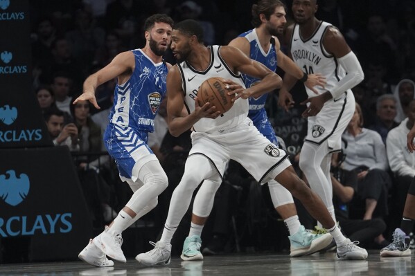 Brooklyn Nets Mikal Bridges, center, holds onto the ball while being defended during a preseason NBA basketball game against Israel's Maccabi Ra'anana, Thursday, Oct. 12, 2023, in New York. (AP Photo/Bebeto Matthews)