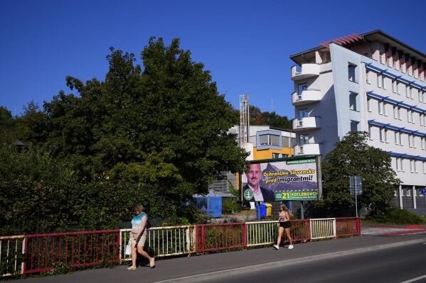 People pass by an election billboard of far-right "Kotlebovci" party in Banska Bystrica, Slovakia, Wednesday, Sept. 6, 2023. The billboard reads: 'We will save Slovakia from migrants'. Slovakia holds early parliamentary elections on Saturday Oct. 30, 2023, with a populist former prime minister Robert Fico and his scandal-tainted party "SMER" (Direction) favored to win after campaigning on a clear pro-Russian and anti-American message. (AP Photo/Petr David Josek)