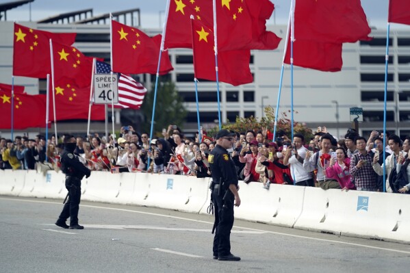 With American and Chinese flags flying, people watch as the motorcade carrying President Joe Biden drives past Tuesday, Nov. 14, 2023, in San Francisco. (AP Photo/Evan Vucci)